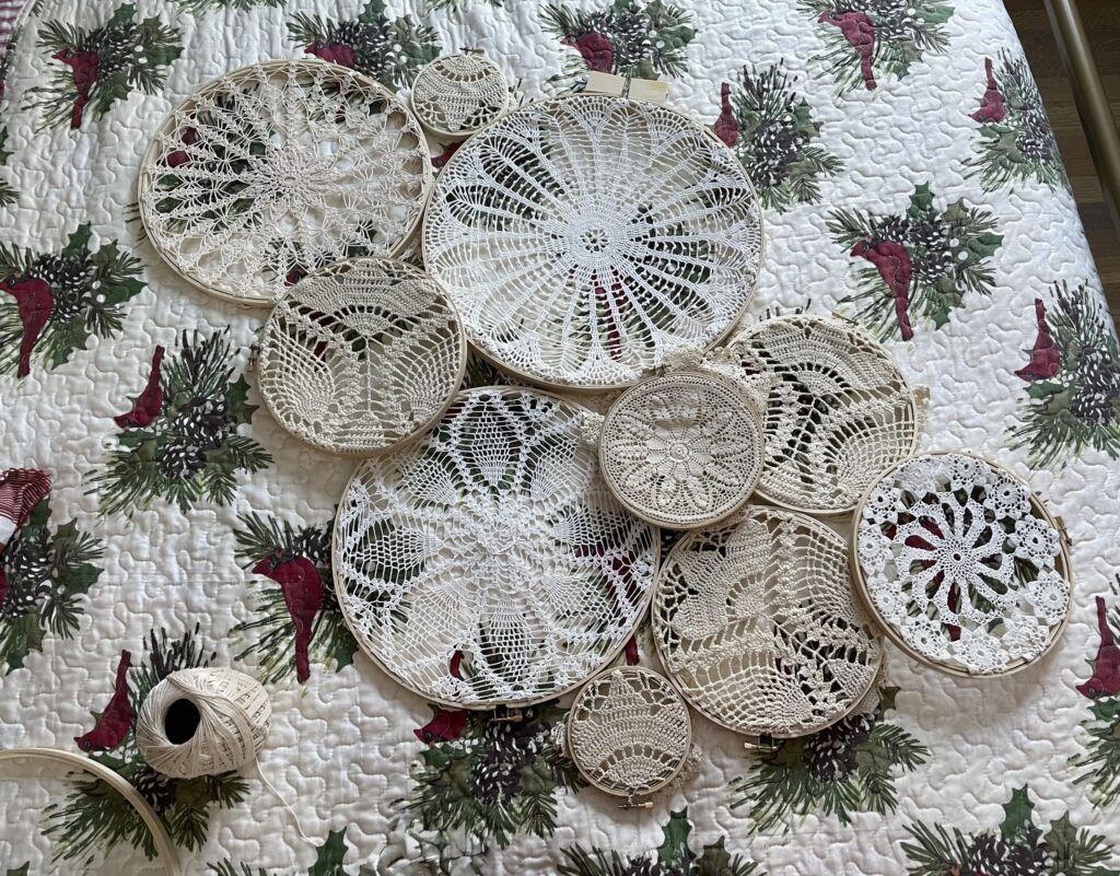 Doilies in hoops arranged on a cardinal bedspread with a twine roll and empty hoop sitting beside it.